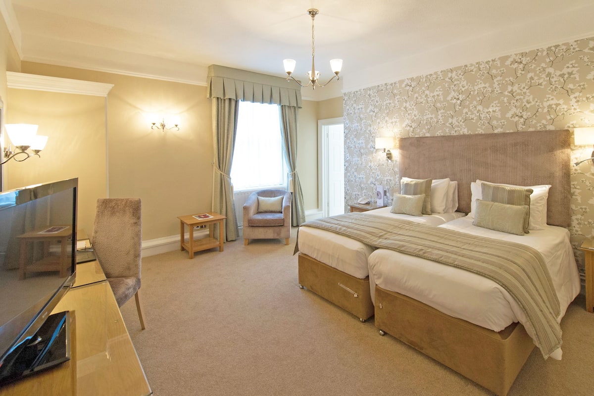 Quarto de hotel com uma cama grande, televisão, cadeira e escrivaninha.
