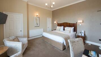 A hotel room with a large bed, two armchairs, a bedside table with a lamp, and a wall-mounted TV.