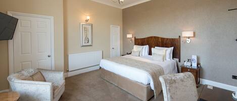 A hotel room with a large bed, two armchairs, a bedside table with a lamp, and a wall-mounted TV.