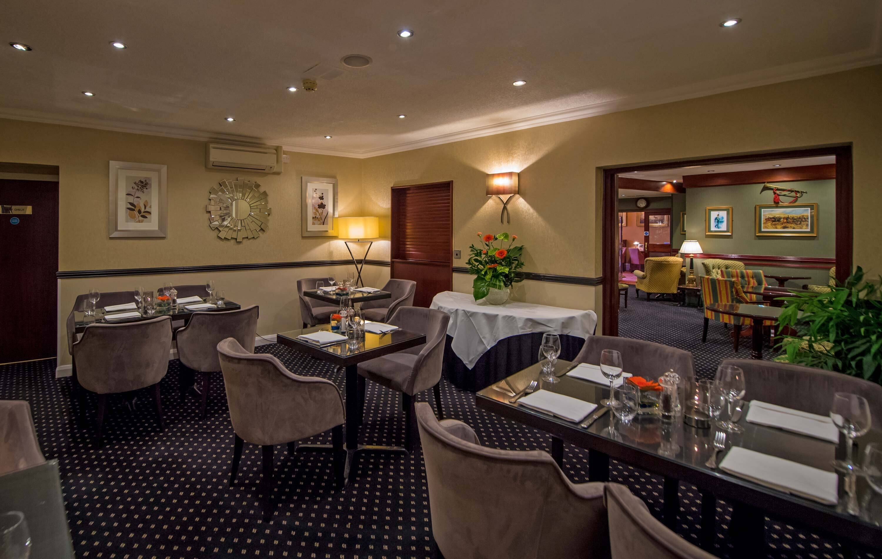 A hotel dining area with tables set for four, chairs, and a decorative wall clock.