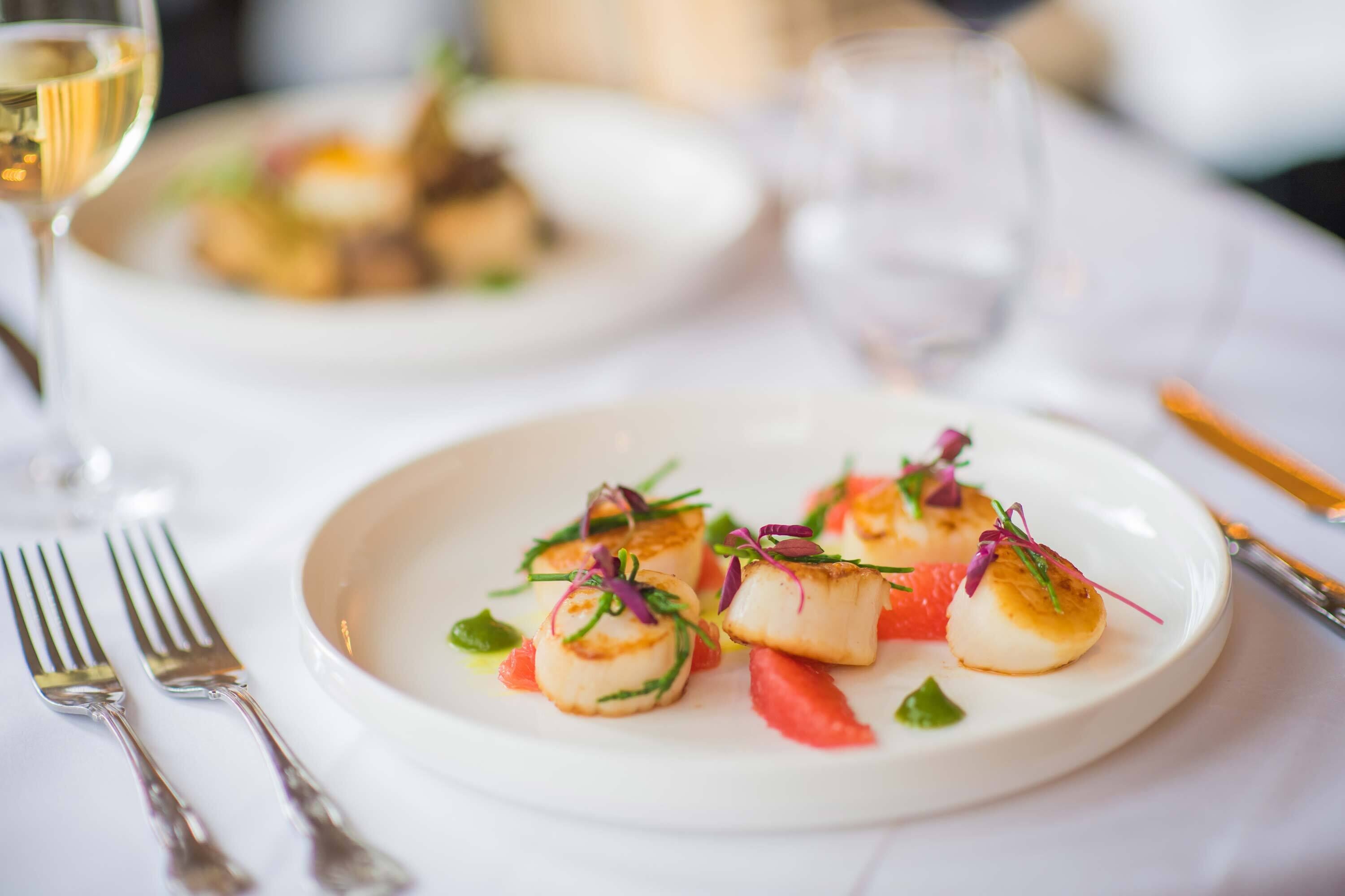 A plate of seared scallops with garnishes on a white plate.