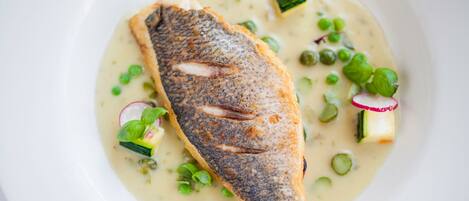 Un plato blanco con un pescado a la parrilla, guisantes verdes, rodajas de rábano y calabacín.