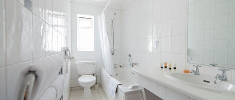 A modern bathroom with white tiles, a toilet, a shower, a sink, and a mirror.