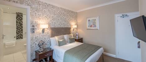A hotel room with a shower, a bed with multiple pillows, two bedside tables, a wall-mounted TV, and a door.