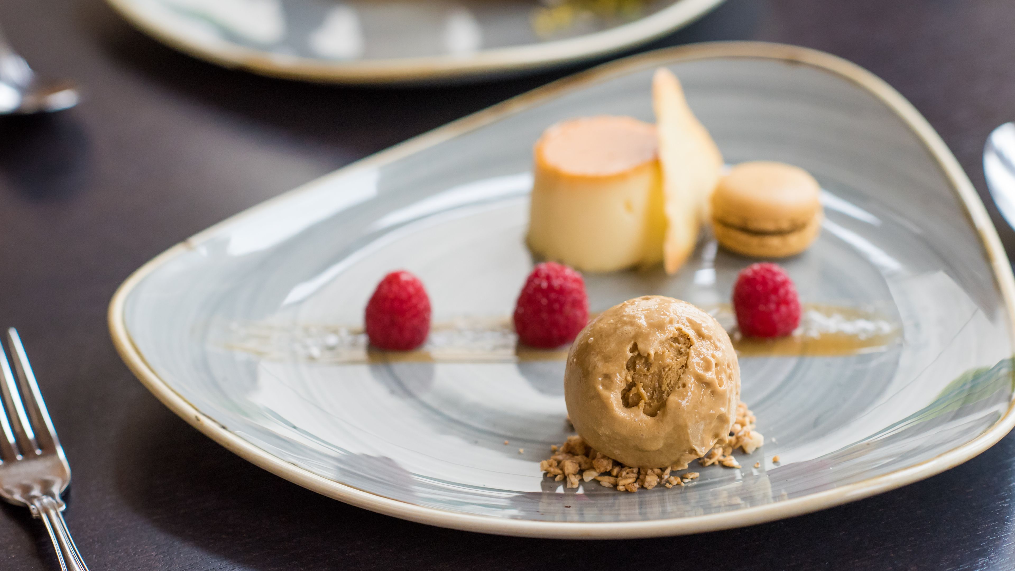 Une assiette de dessert avec une boule de glace, des framboises et des macarons.