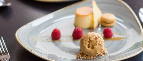Une assiette de dessert avec une boule de glace, des framboises et des macarons.