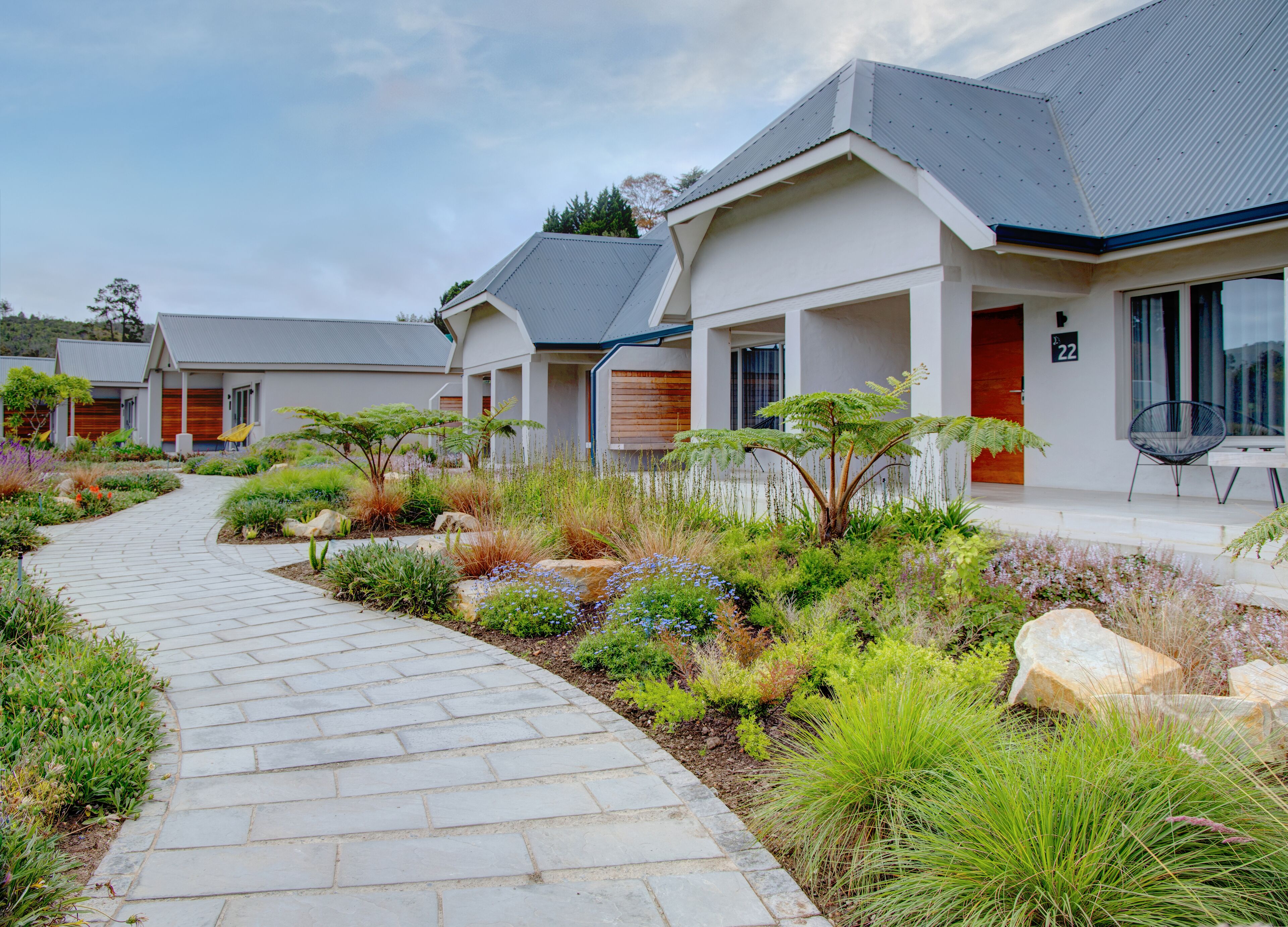 A pathway leading to a row of modern houses with a well-maintained garden and a clear sky.