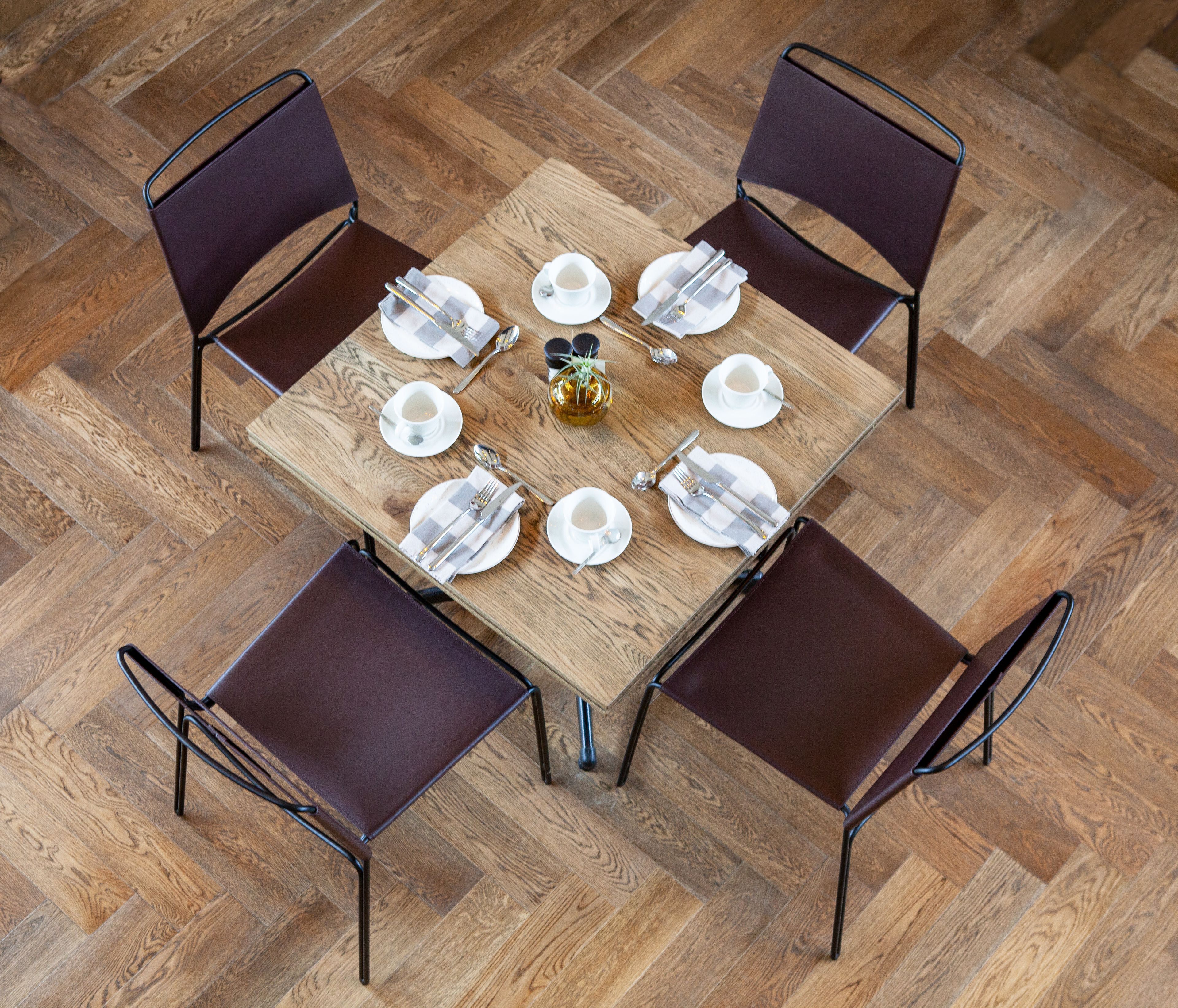A square wooden table with a central vase, surrounded by four chairs with metal frames.