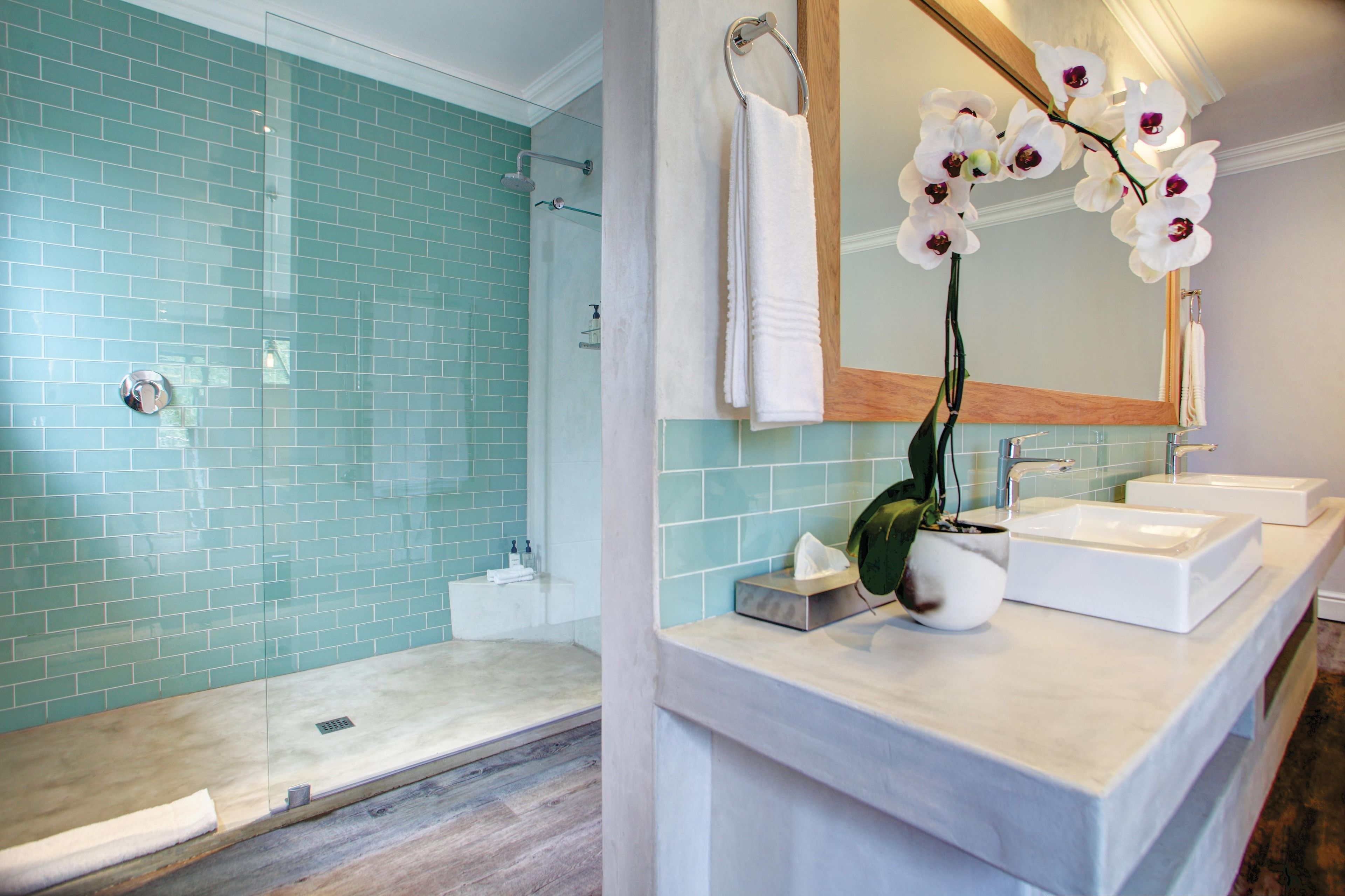 A modern bathroom with a glass shower enclosure, a white sink, and a mirror with an orchid plant.