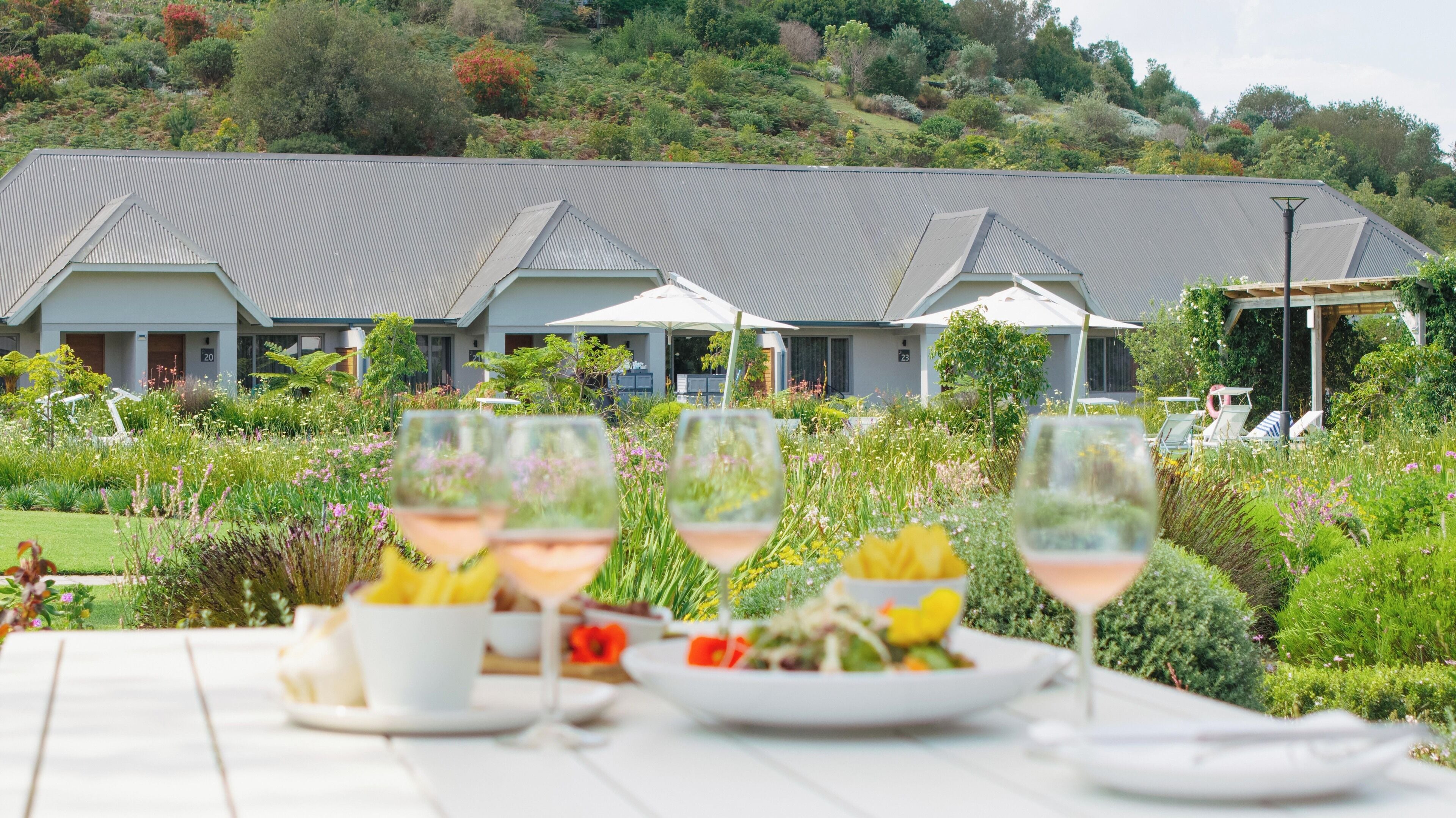 Un espace repas avec des sièges en plein air, une vue sur un bâtiment avec un toit gris et un jardin luxuriant en arrière-plan.