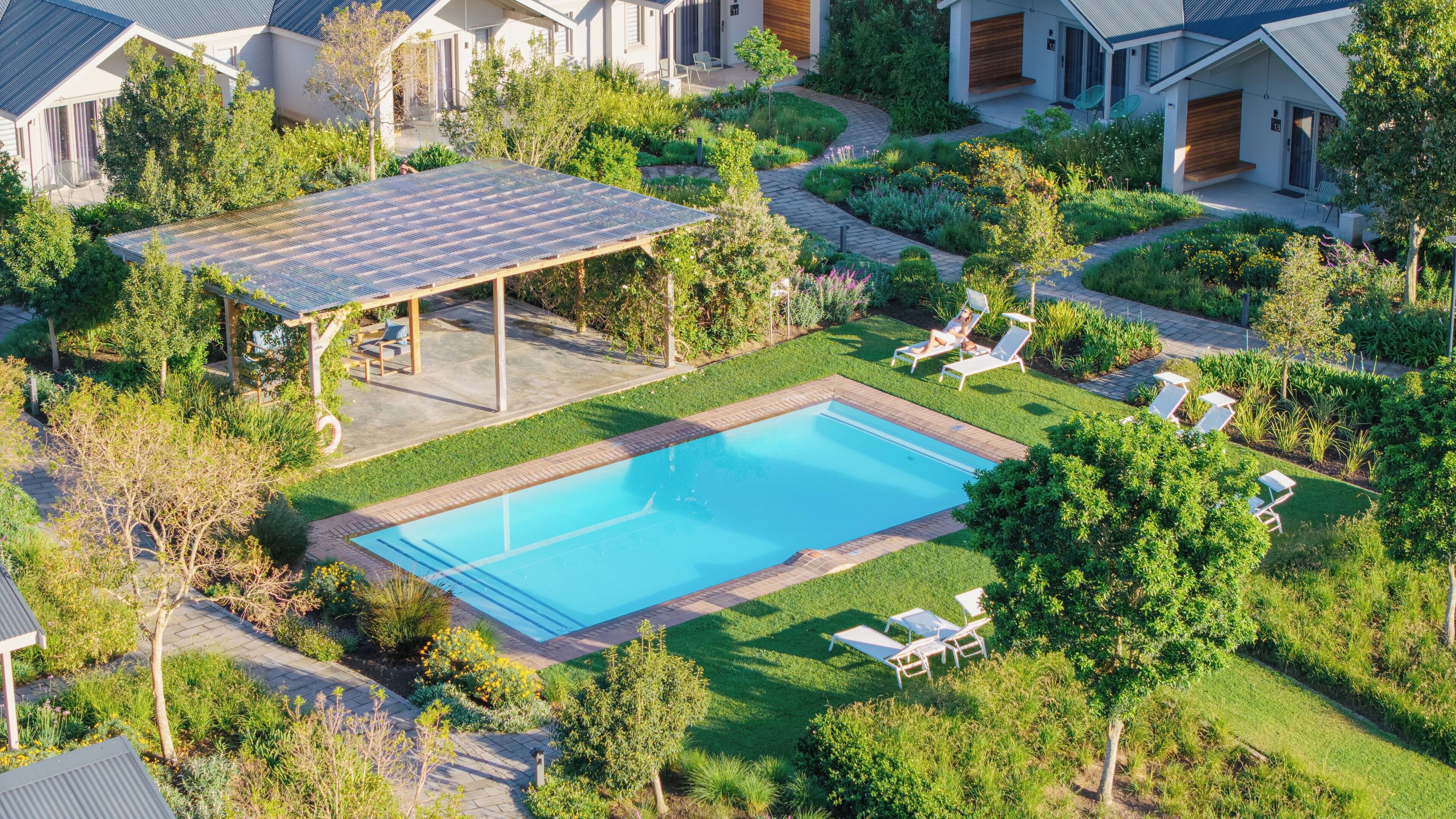 A residential area with a swimming pool, lounge chairs, and a covered patio.