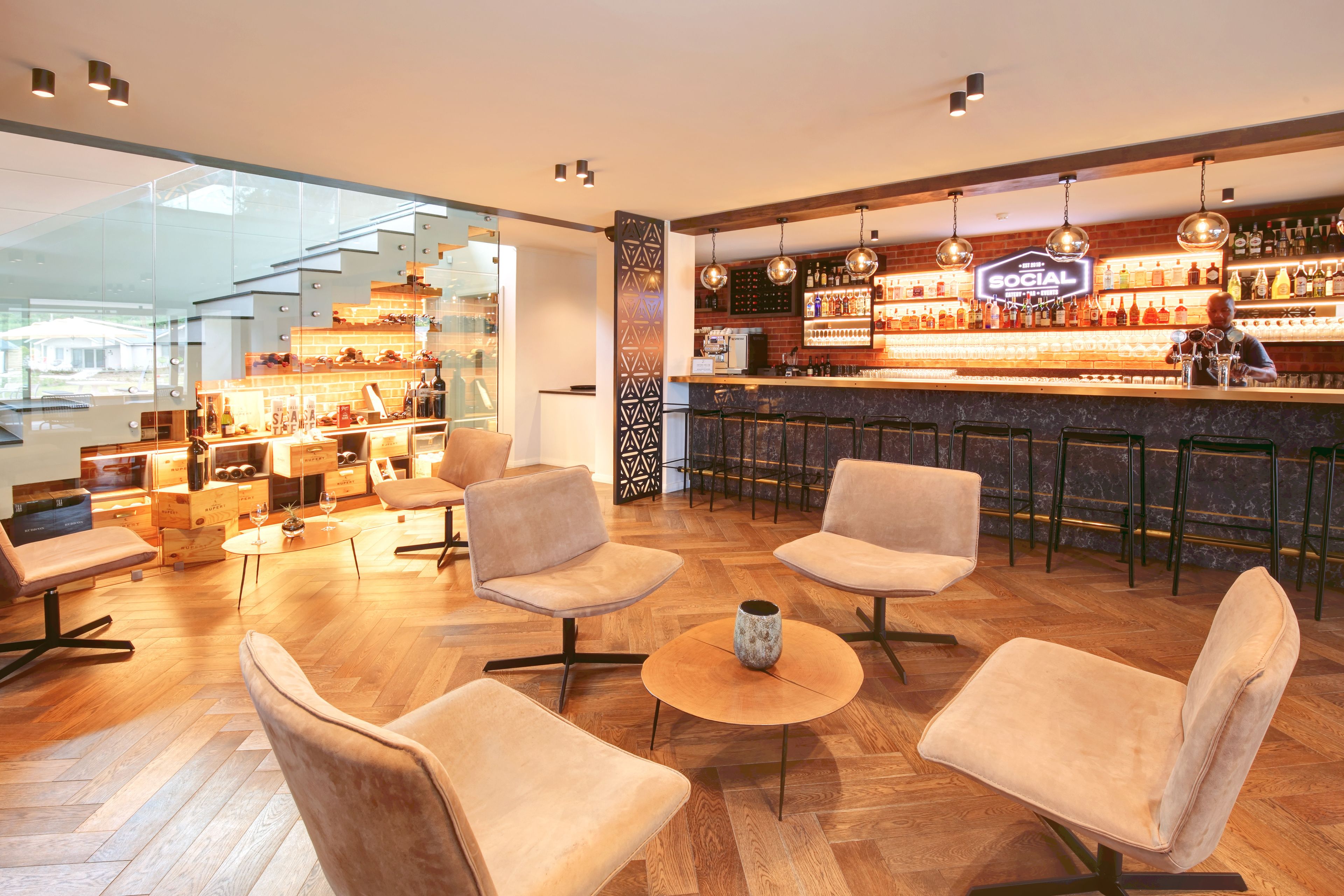 A modern bar area with wooden flooring, cushioned seating, and a well-stocked bar counter.