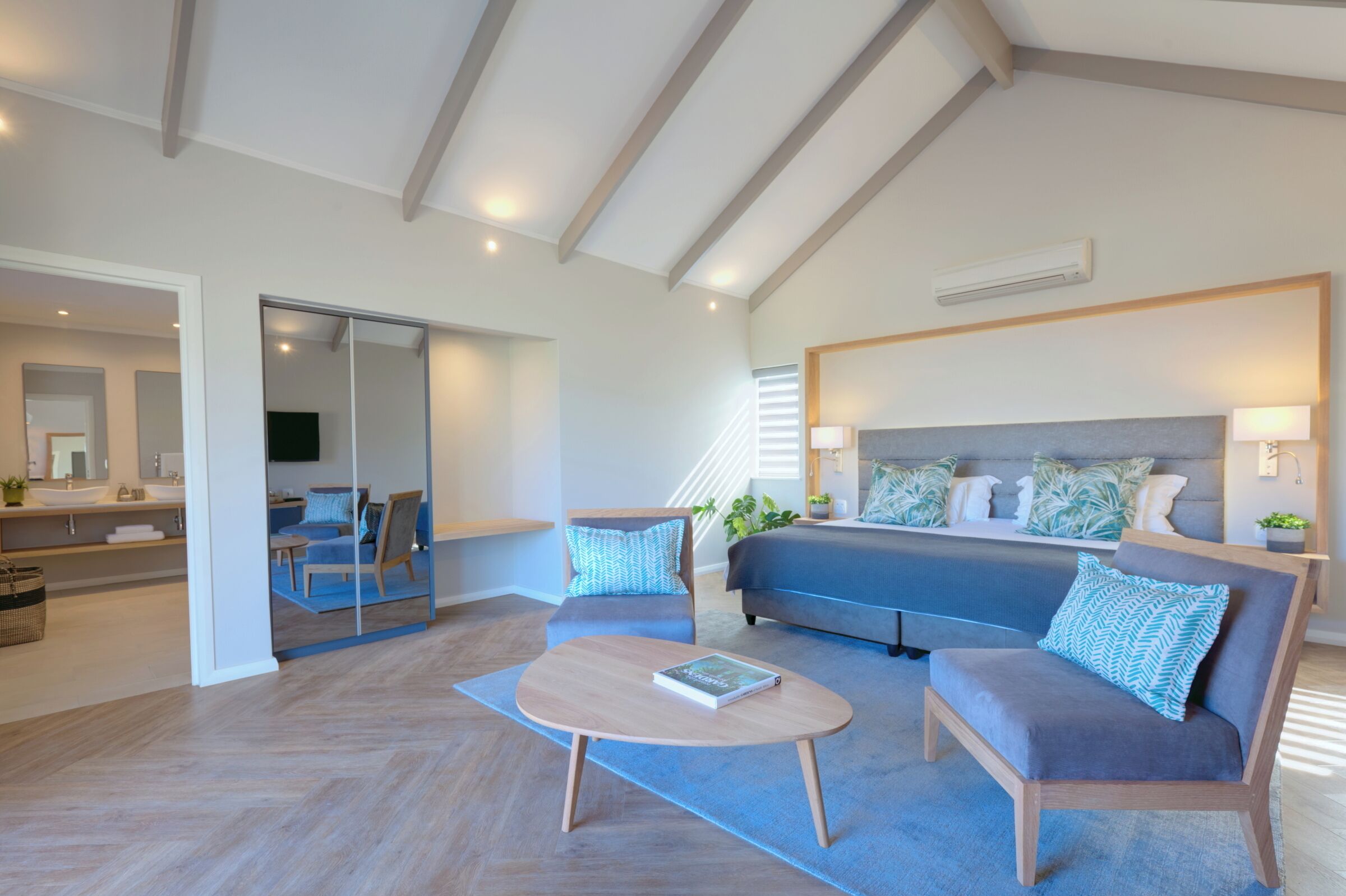 Une chambre moderne avec un grand lit, un canapé, une table basse et une porte-fenêtre coulissante donnant sur une salle de bain.