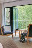Una habitación con un ventanal grande, balcón y vistas al verdor.