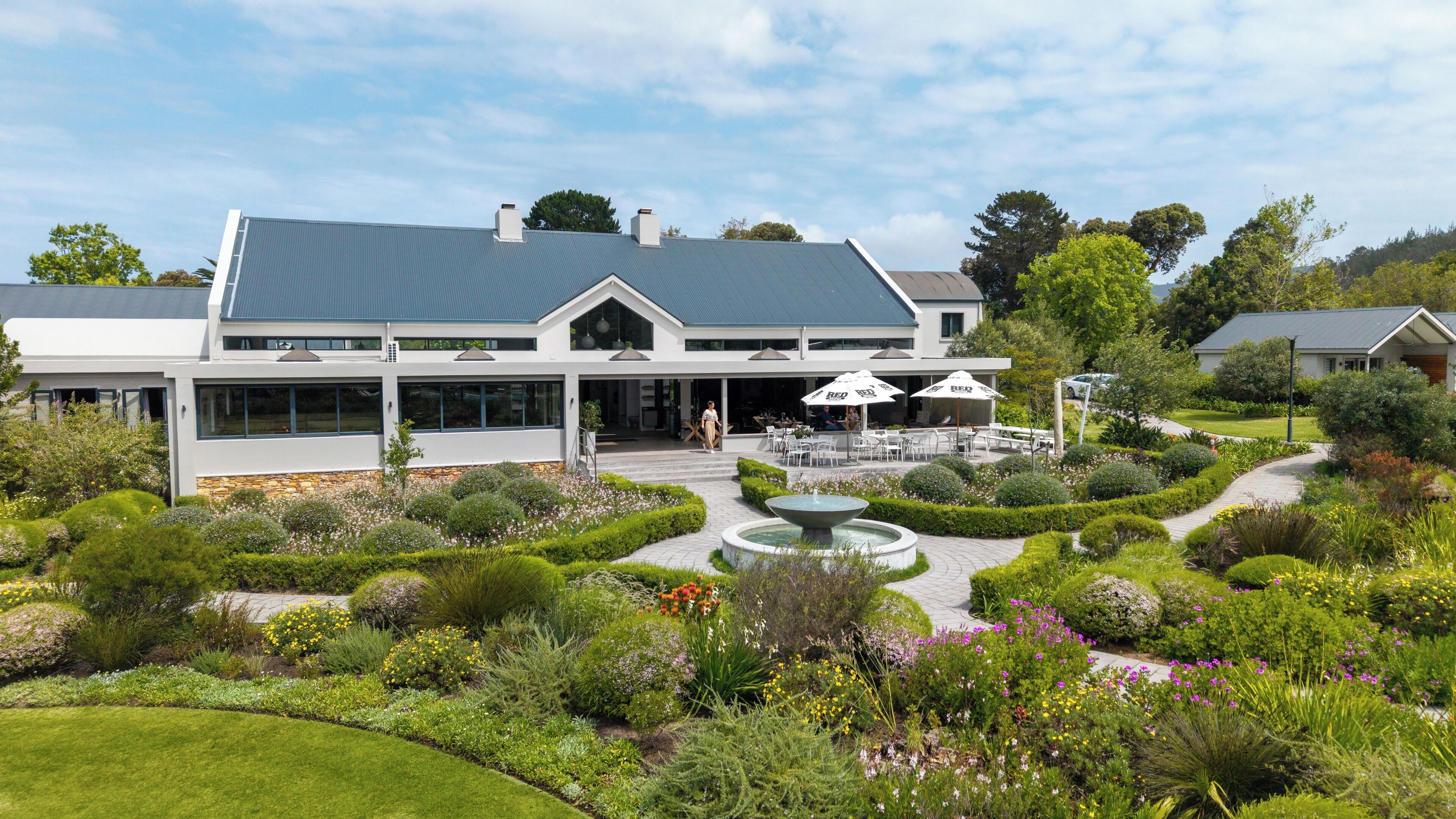 A modern two-story building with a covered outdoor seating area and a well-maintained garden with a fountain.