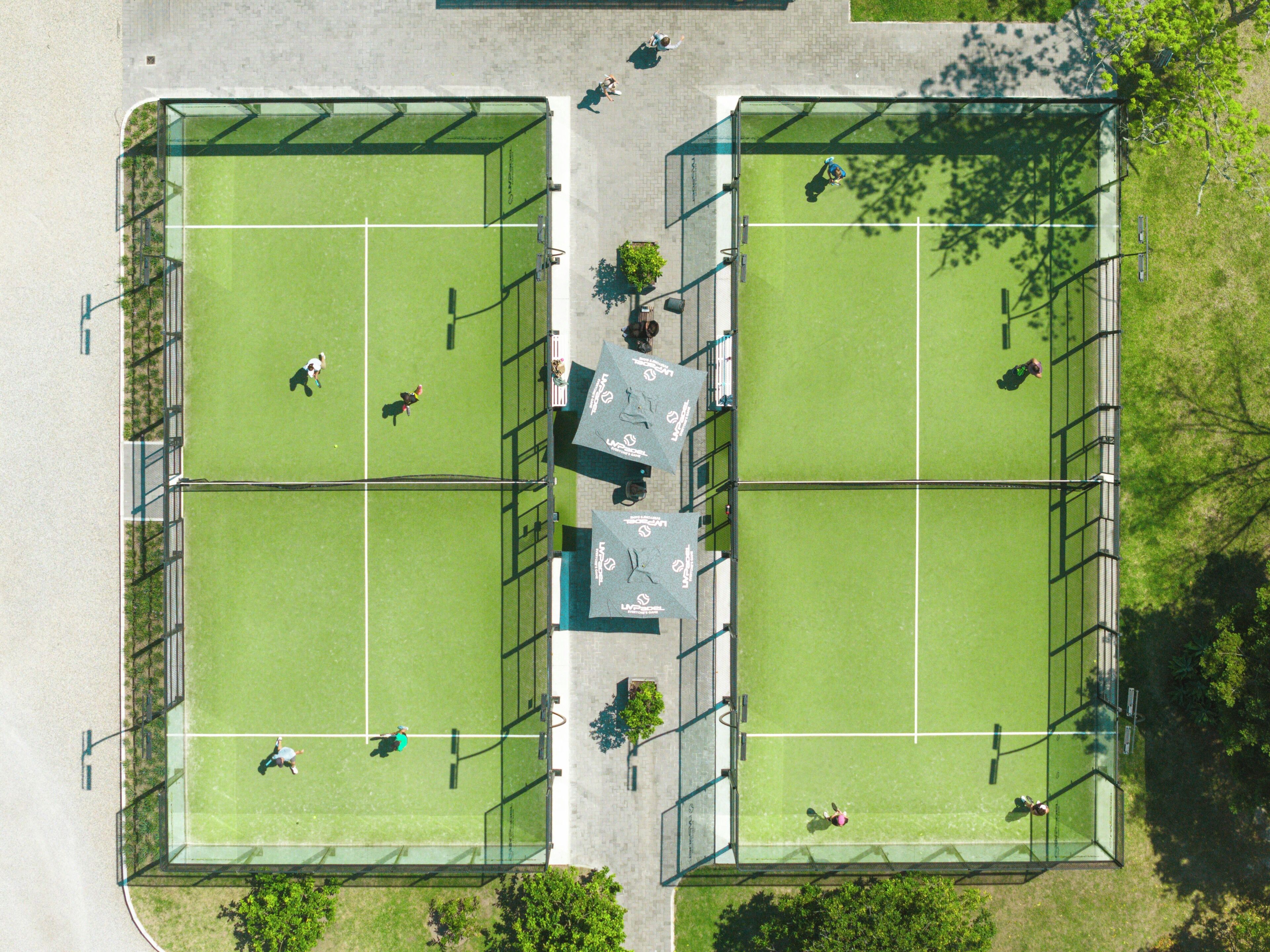 An aerial view of a tennis court complex with two courts, fencing, and trees.