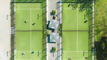 An aerial view of a tennis court complex with two courts, fencing, and trees.
