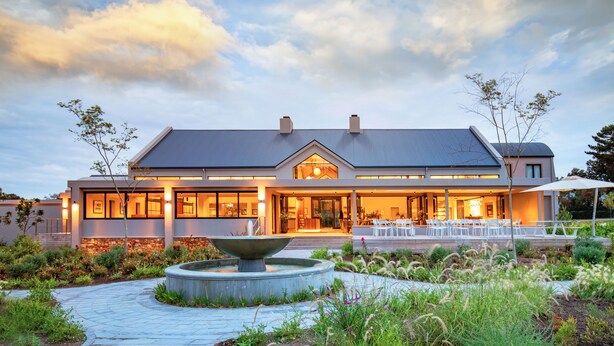 A modern two-story building with a large entrance, outdoor seating area, and a central water feature. - Knysna Hollow Country Estate (Knysna)