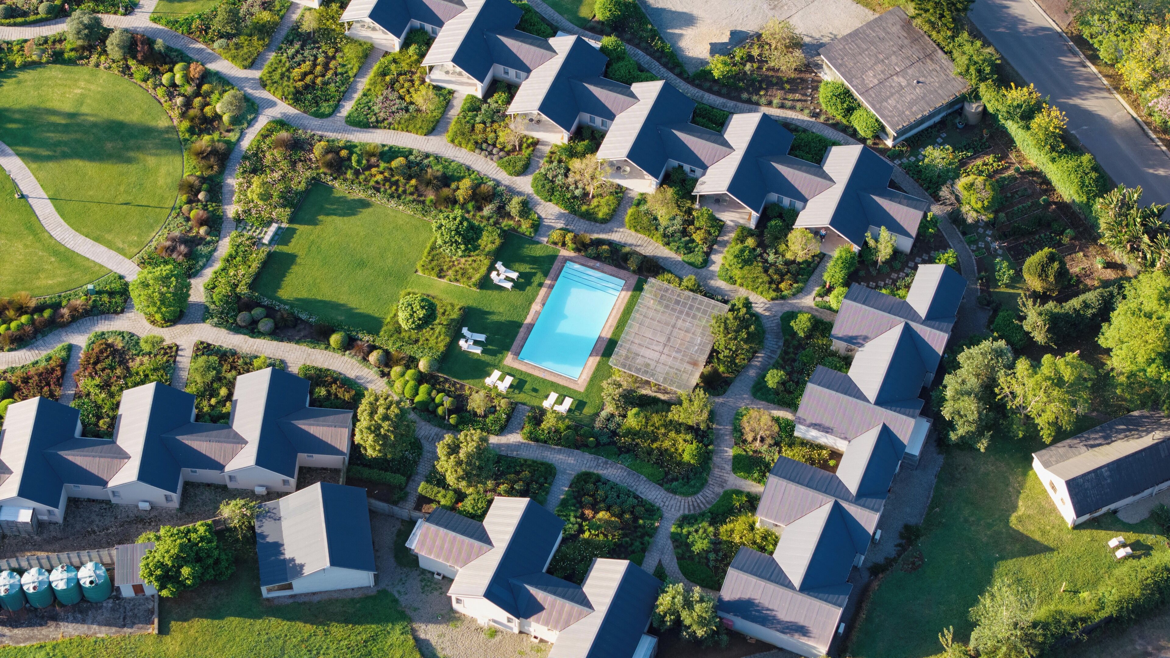 An aerial view of a residential area with multiple houses, a swimming pool, and well-maintained gardens.