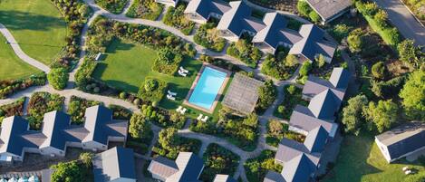 An aerial view of a residential area with multiple houses, a swimming pool, and well-maintained gardens.