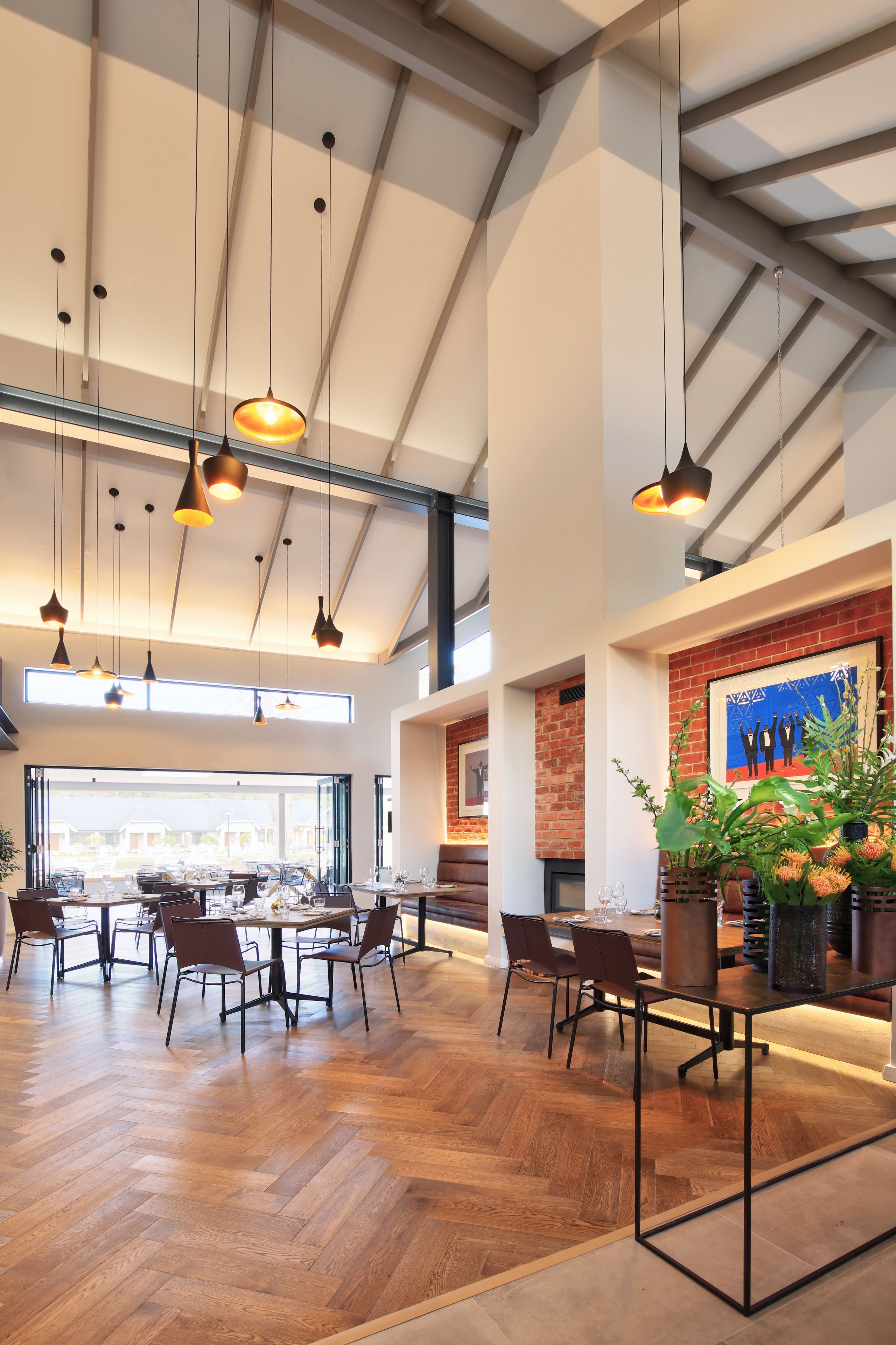 A spacious dining area with wooden flooring, modern pendant lighting, and a brick fireplace.