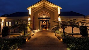A modern building with a wooden pathway leading to a glass entrance, surrounded by tropical plants. - Knysna Hollow Country Estate (Knysna)