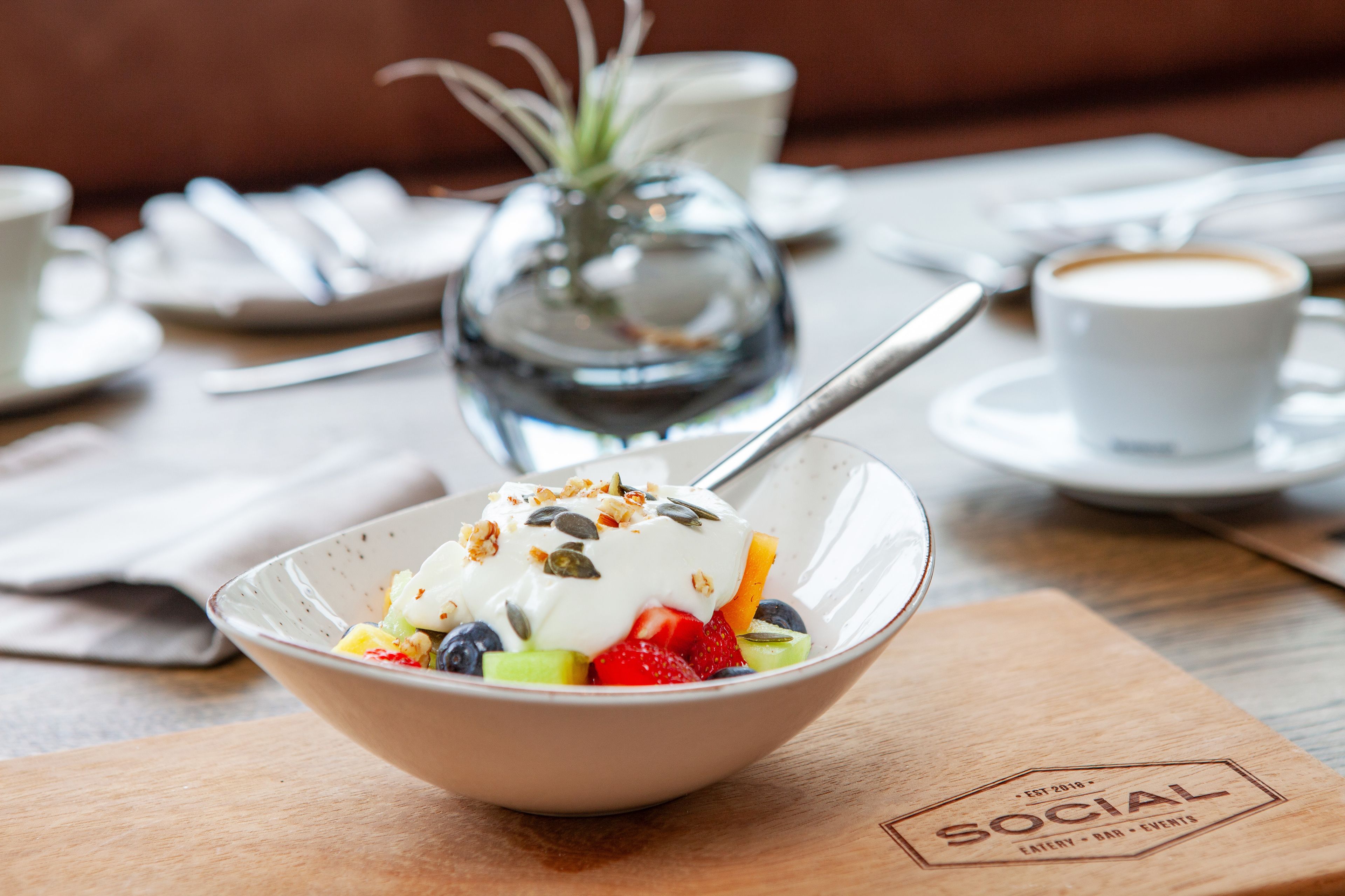 A bowl of fruit salad with yogurt and granola on a wooden table.