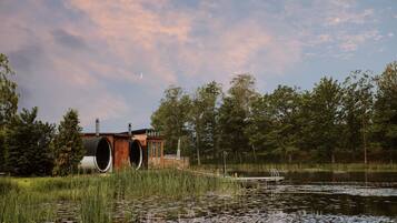 Una cabaña junto al lago con un muelle, rodeada de pastos altos y árboles.