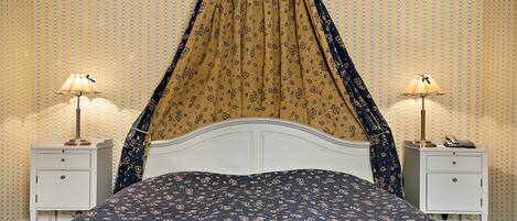 Un dormitorio con cama, dos mesitas de noche, dosel y papel tapiz estampado.