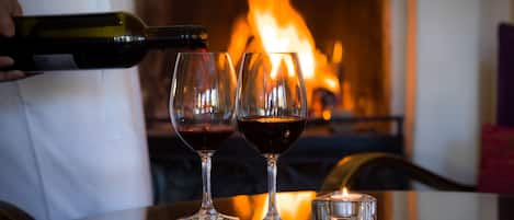 Una mesa con dos copas de vino, una vela y una botella de vino siendo servida.