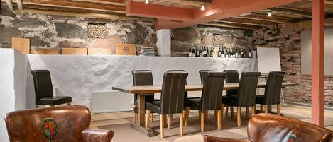 A rustic dining area with a brick wall, wooden ceiling beams, and leather chairs.