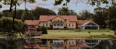 A large house with a red roof, a pond in front, and a reflection of the house.