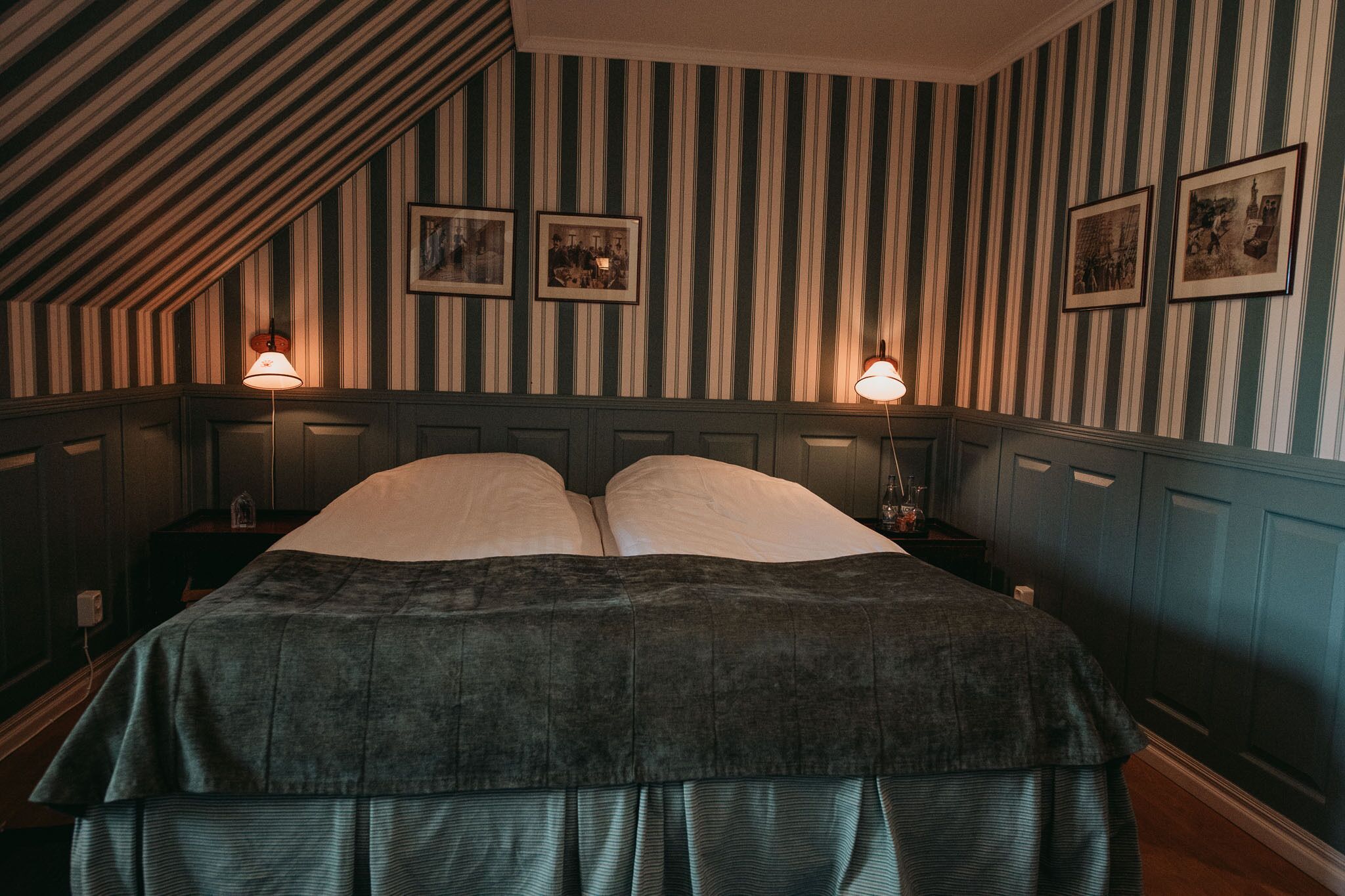 A room with a large bed, striped wallpaper, and framed pictures on the wall.