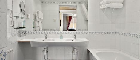 Un baño con un lavabo blanco, dos llaves, un espejo y una bañera.