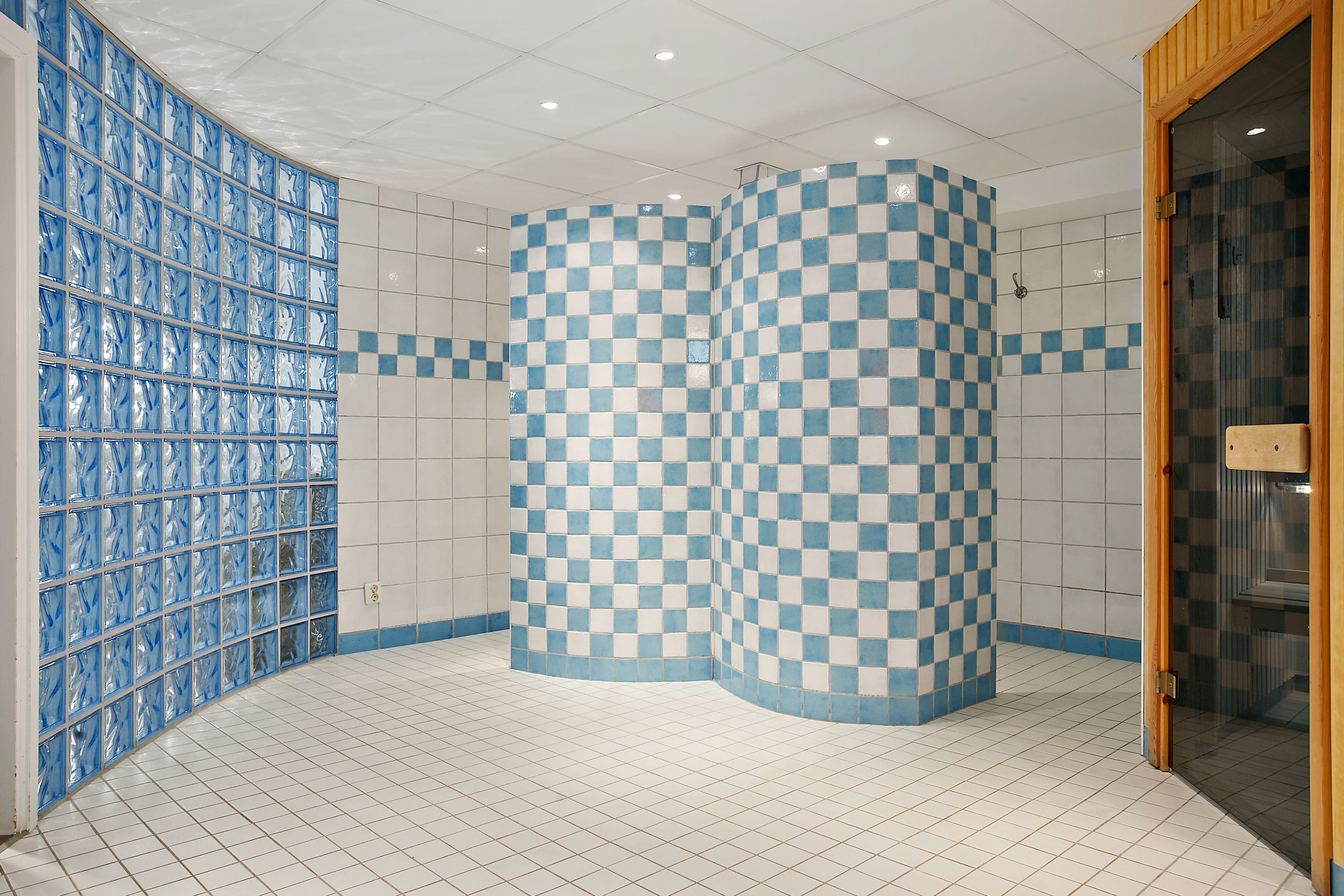 A bathroom with a checkered tile wall, a glass partition, and a tiled floor.