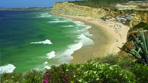 A coastal beach with clear waters, sandy shore, and a cliffside with buildings. -  Boutique Hotel Vivenda Miranda (Lagos)