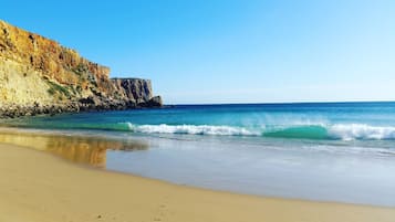 Une plage avec une eau d’un bleu limpide, un rivage sablonneux et des falaises rocheuses.