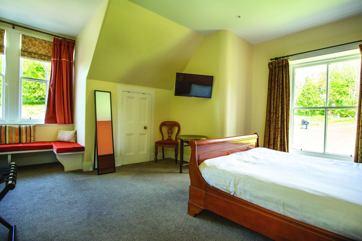 A bedroom with a bed, a chair, a television, a window with curtains, and a bench by the window.