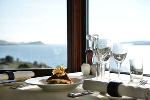 A table set for dining with a plate of food, glasses, and a view of the sea. - Loch Melfort Hotel (Oban)