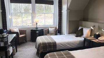 A hotel room with two beds, a desk, a chair, and a view of the outdoors.