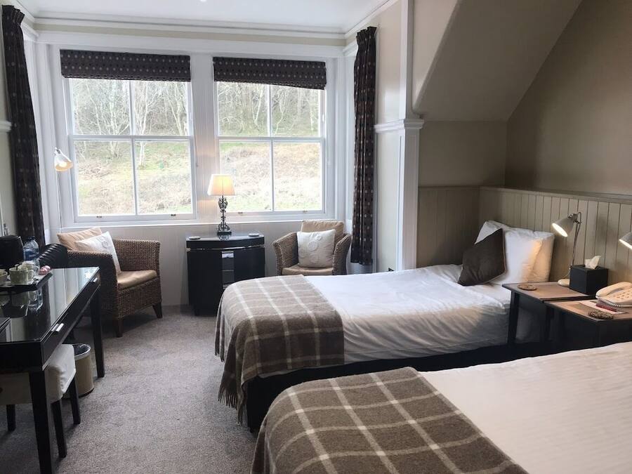 A hotel room with two beds, a desk, a chair, and a view of the outdoors.