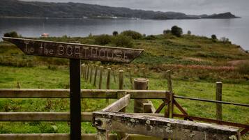 A wooden signpost with the inscription "To the BOATHOUSE" in a rural setting with a body of water and hills in the background.