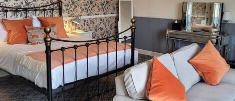 A bedroom with a double bed, a sofa, a chandelier, and a mirror.