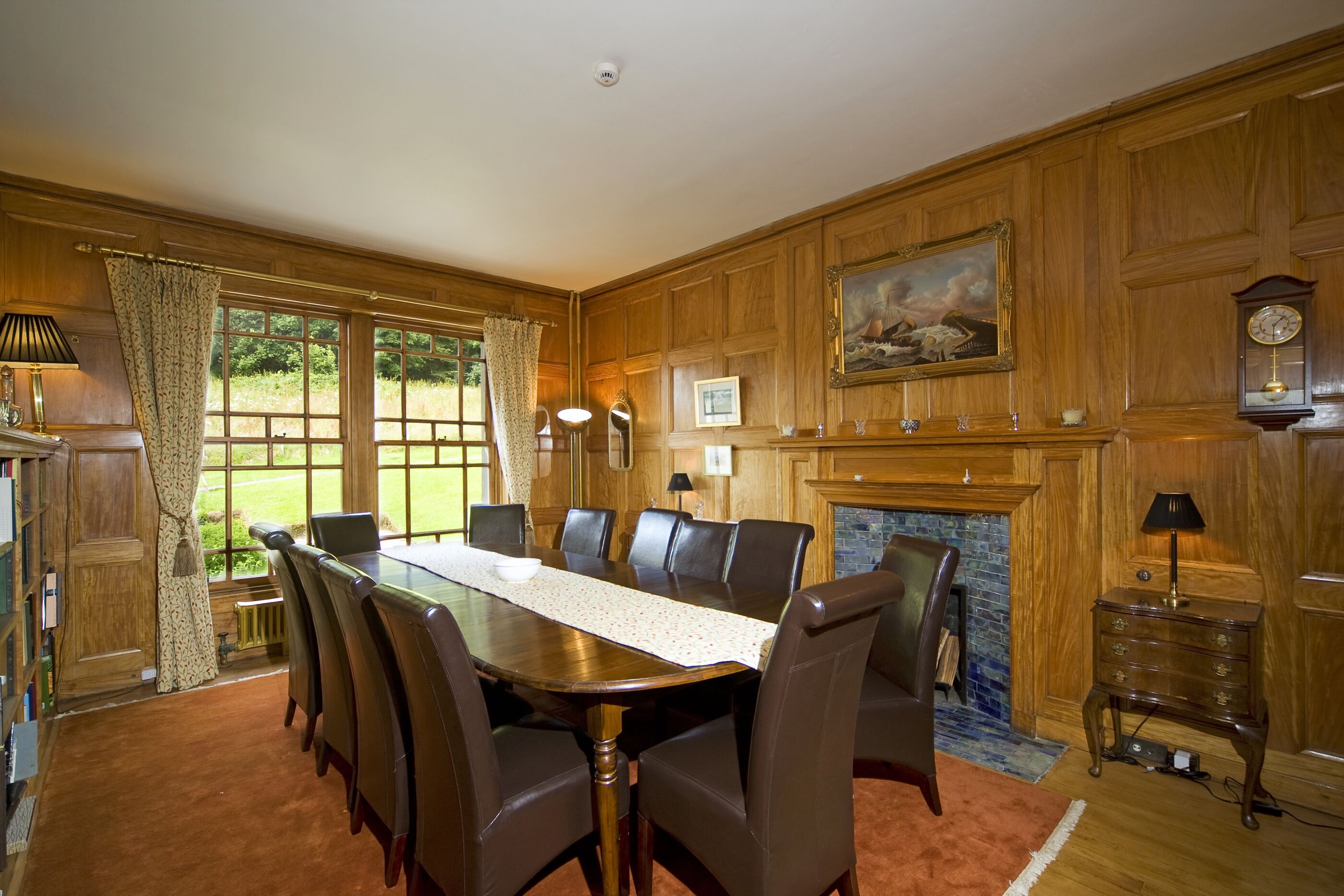 A formal dining room with a large wooden table, leather chairs, a fireplace, and a clock on the wall.