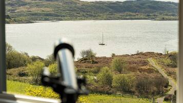 Vista de un lago con un velero, rodeado de colinas y un sendero que lleva a una puerta.