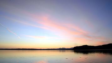Un lago tranquilo al atardecer, con cielo despejado y montañas a lo lejos.