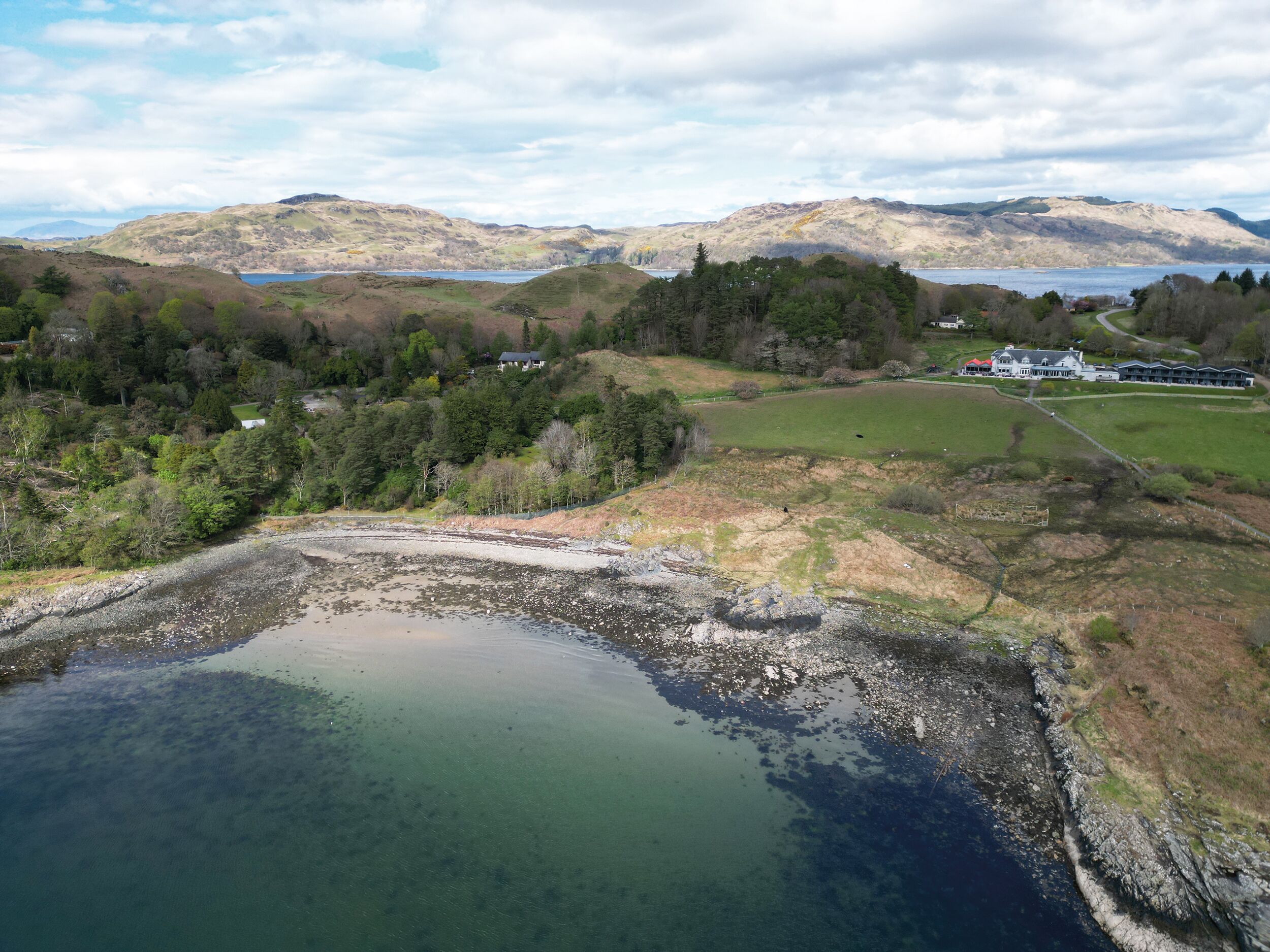 A lakeside property with a large pond, surrounding grassy areas, and a backdrop of hills.