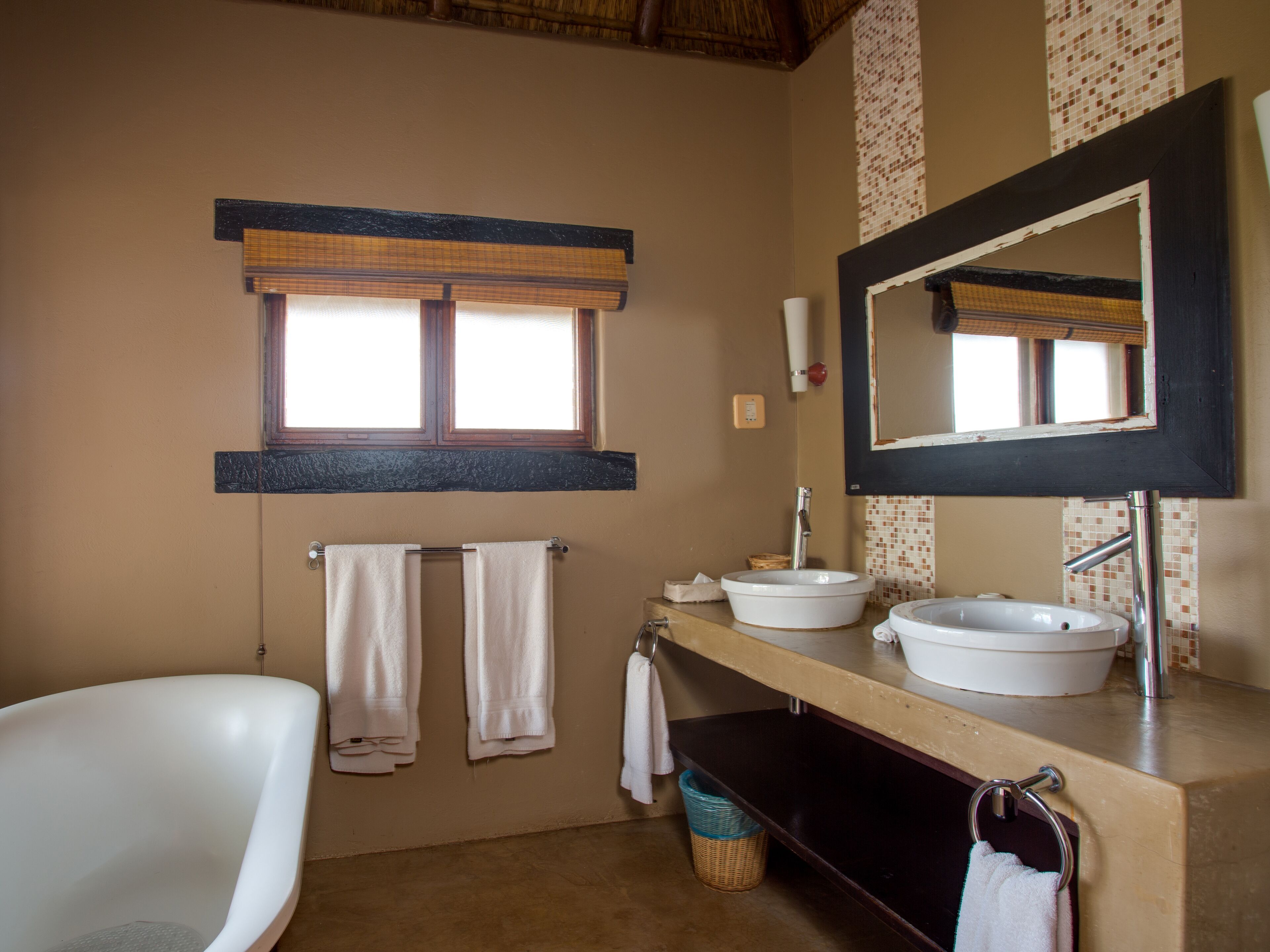 Un baño con bañera, dos lavamanos, un espejo grande y una ventana con persianas.
