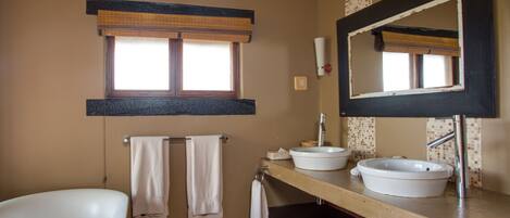 Un baño con bañera, dos lavamanos, un espejo grande y una ventana con persianas.