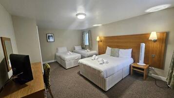 Una habitación de hotel con cama, escritorio, silla, televisor y lámpara.
